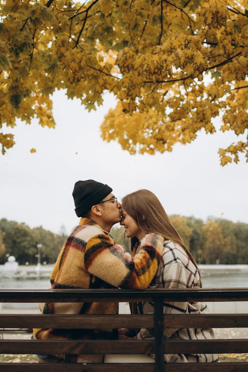 A Man Kissing the Forehead of a Woman While Sitting on a Wooden Bench