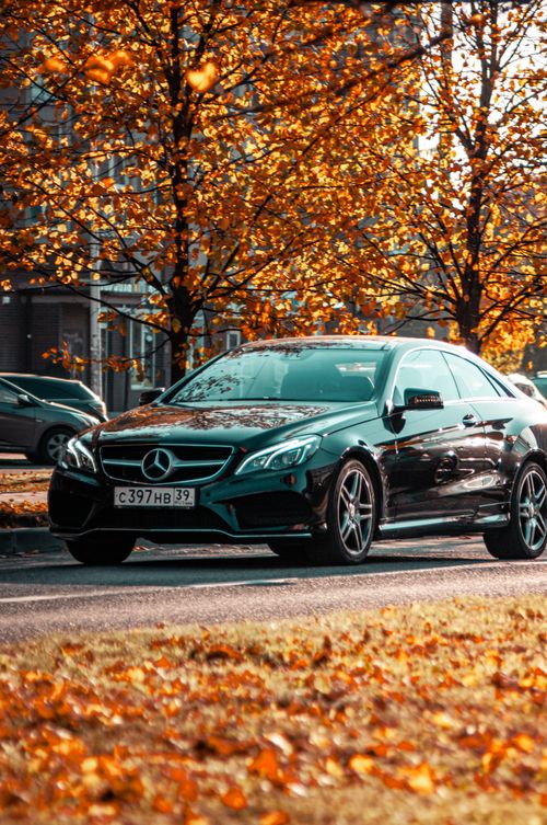 Free Black luxury car on city street during autumn with vibrant orange leaves. Stock Photo