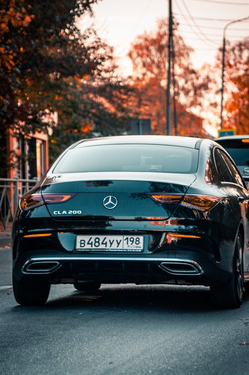 Free Back view of a shiny black Mercedes-Benz CLA car on a city street at dusk with autumn colors. Stock Photo