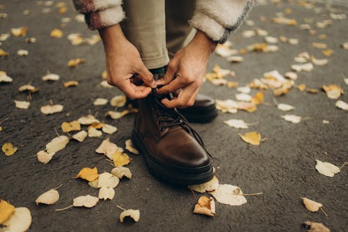 A Person Tying the Lace of His Brown Leather Boots