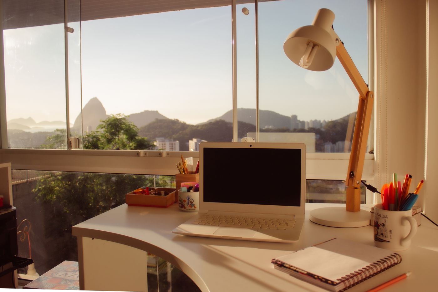A desk and laptop before a window with mountain views
