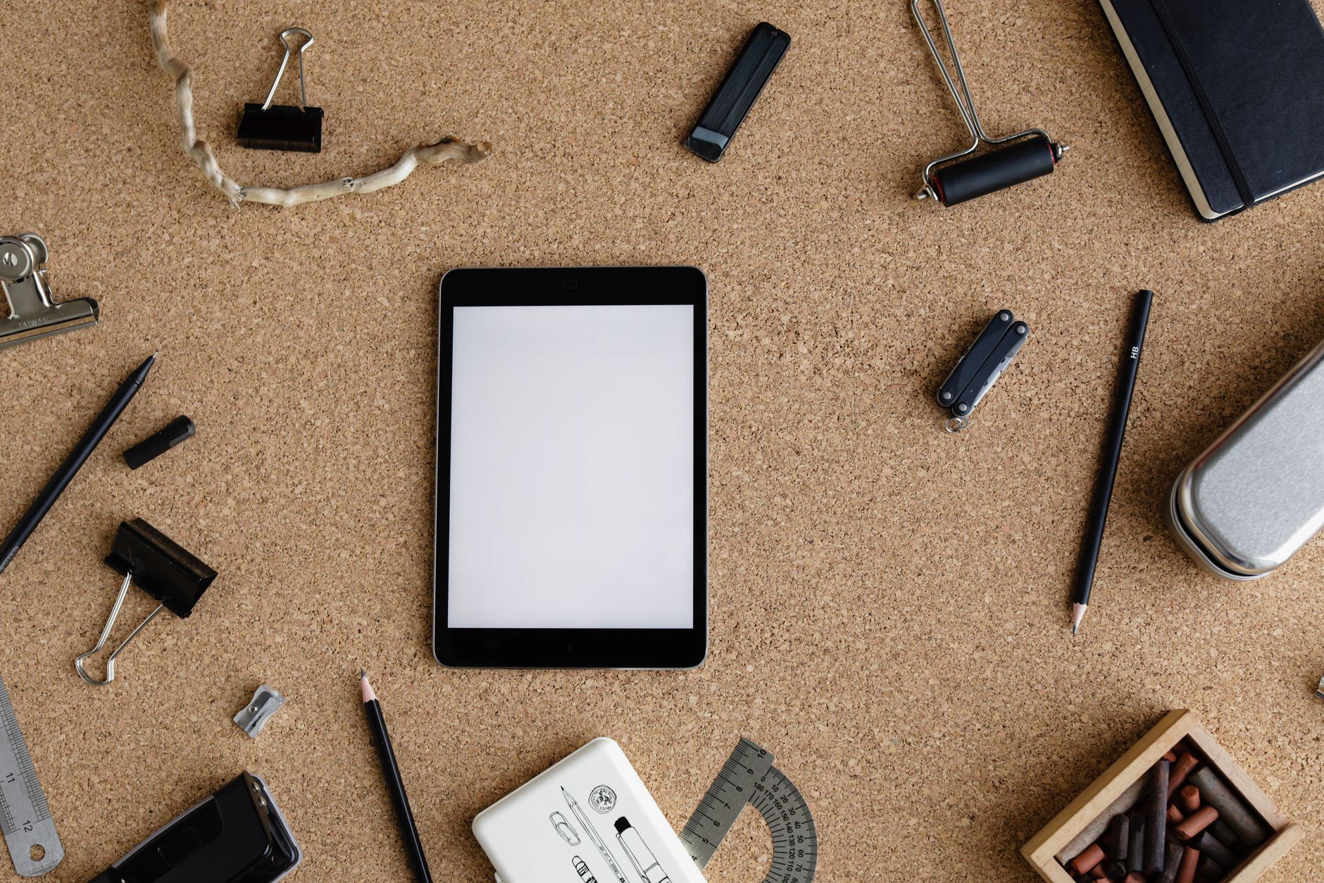 Flat lay of a cork board workspace with various stationery items and a tablet for creative office tasks.