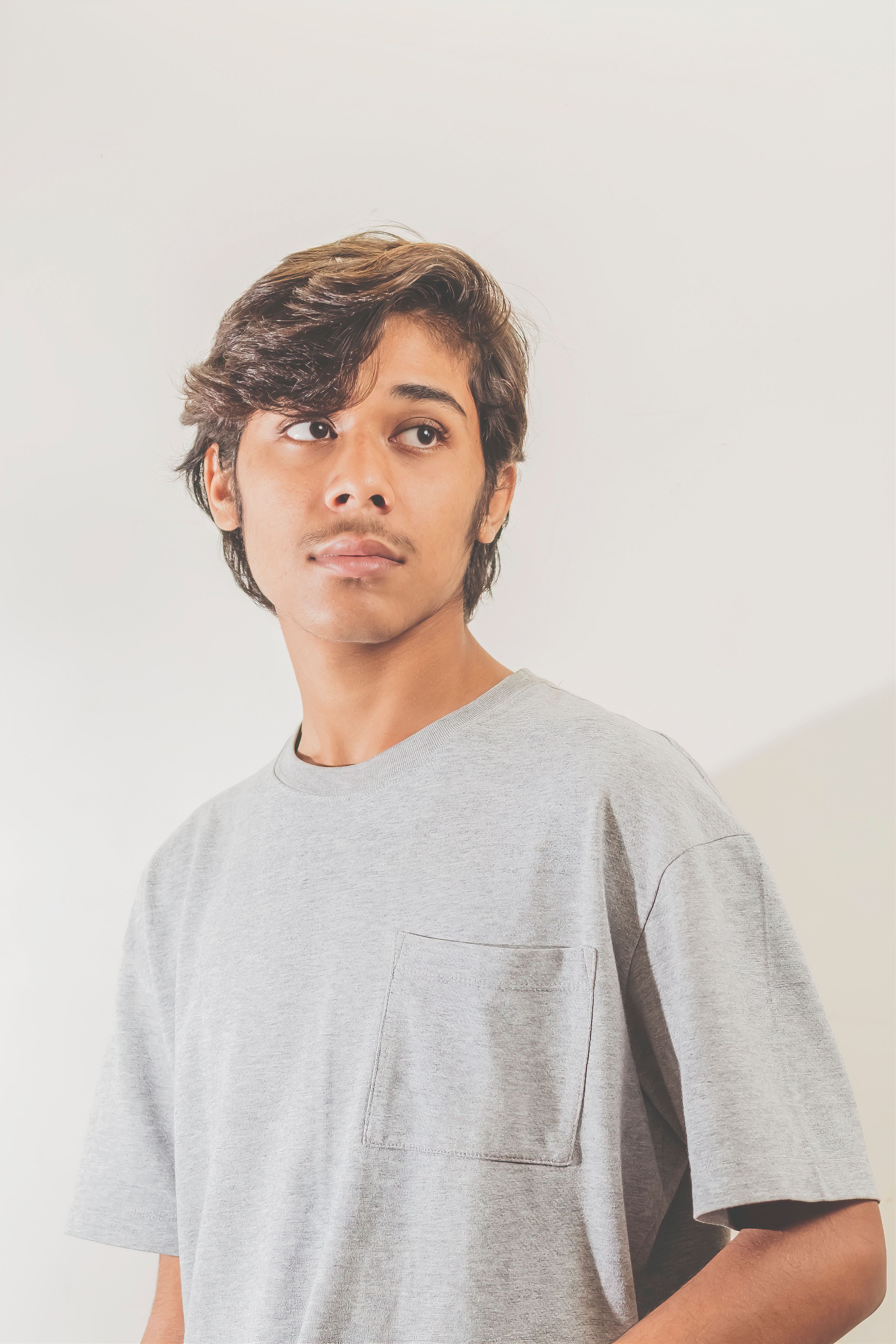 Portrait of a teenager in a gray shirt, gazing thoughtfully away. Bright and neutral background.