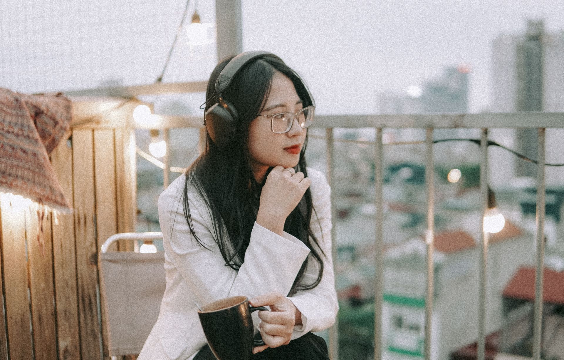 Woman in headphones relaxing with a coffee on a rooftop terrace, enjoying the city view.