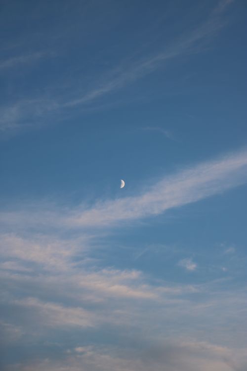 Free A delicate half moon in a clear blue sky with wispy clouds, capturing serene natural beauty. Stock Photo