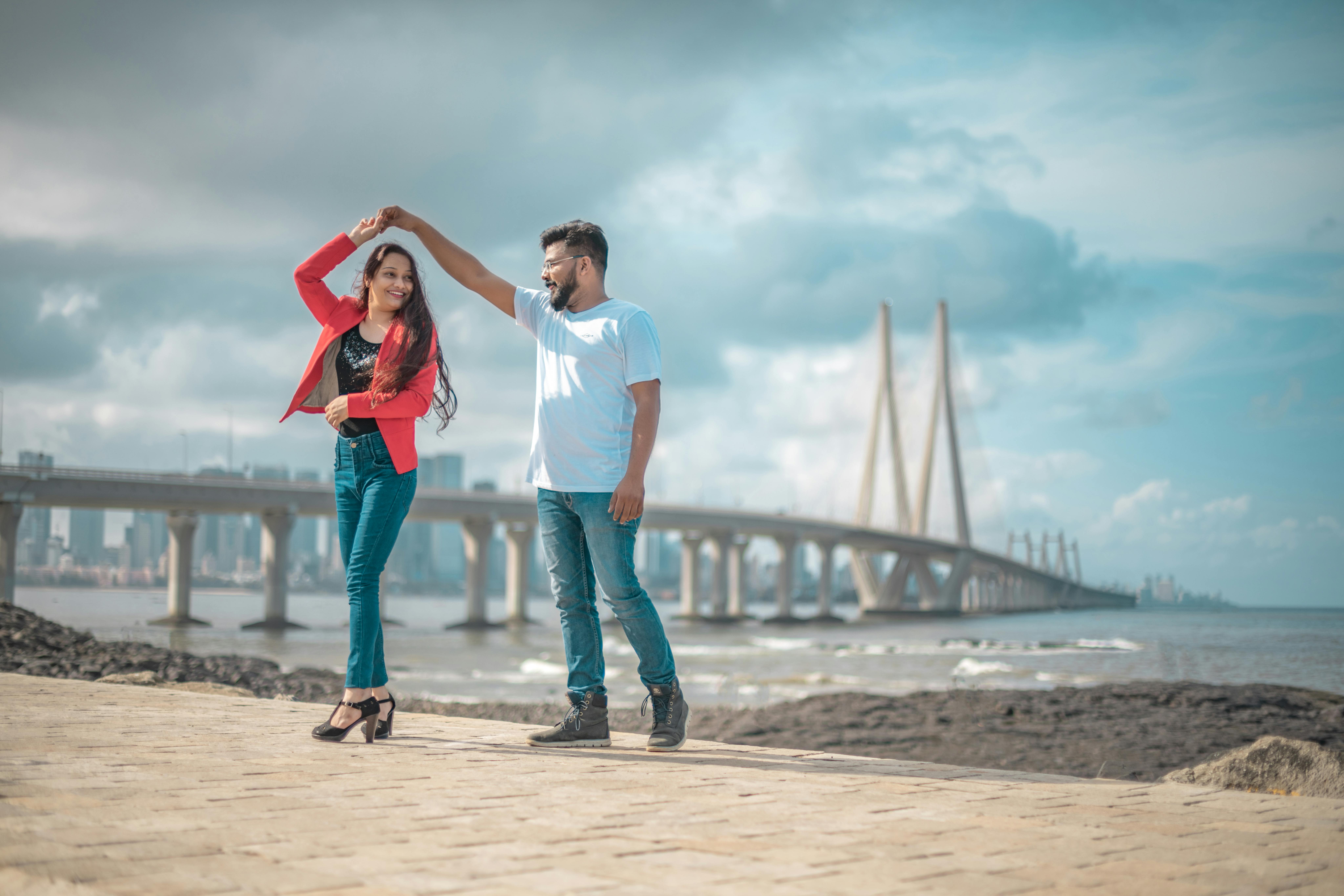 A couple joyously dancing near the iconic Bandra-Worli Sea Link, Mumbai, showcasing love and architecture.