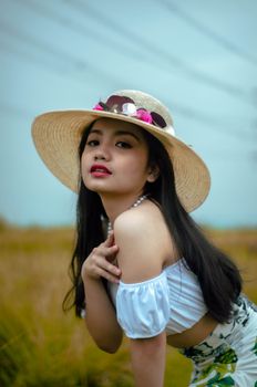 Fashionable woman posing in field wearing straw hat and floral skirt on a sunny day.