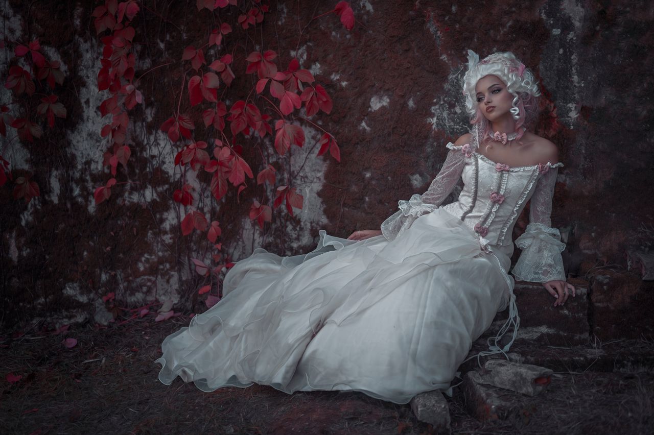 a woman in a vintage white dress poses against a rustic wall with red