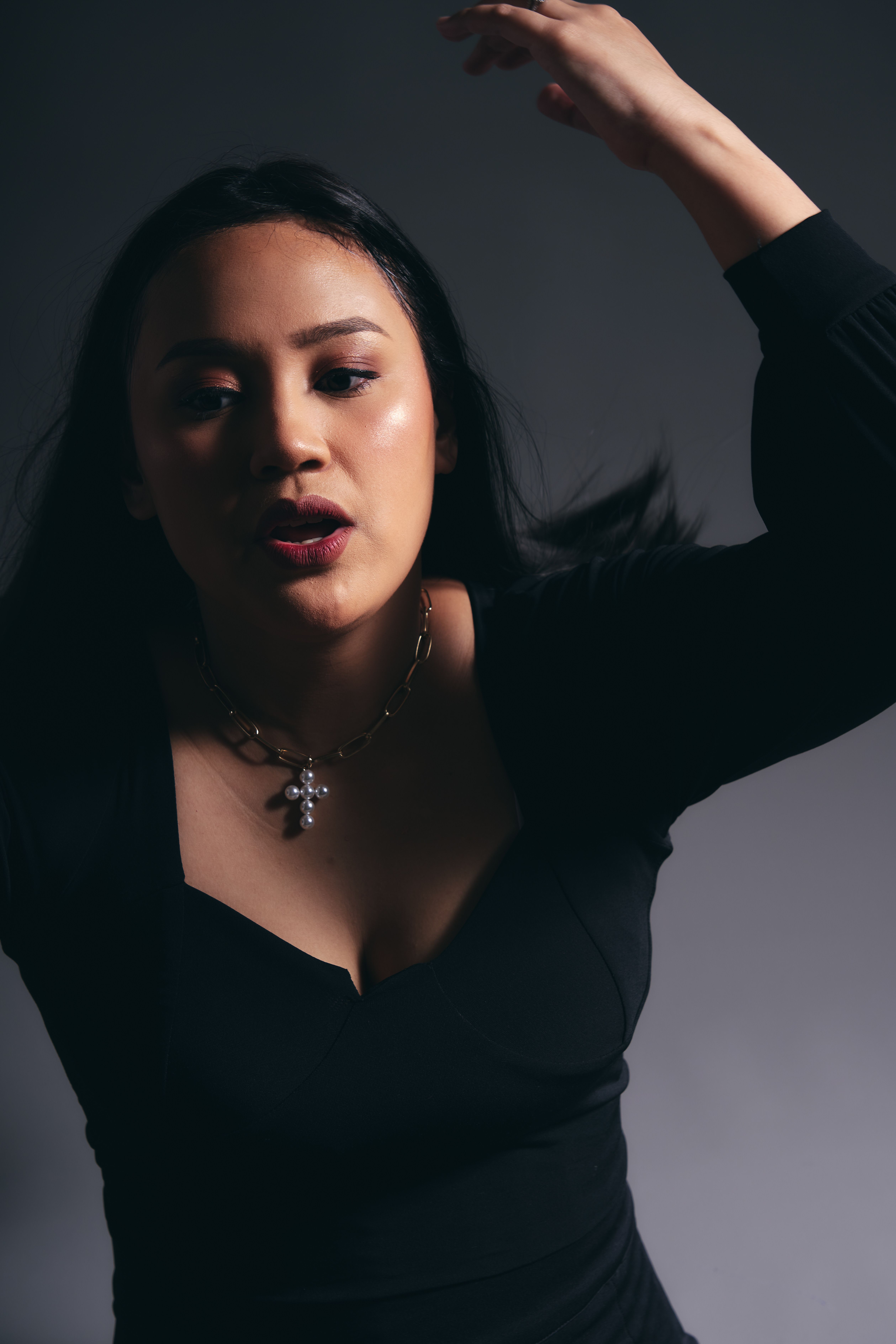 A striking portrait of a young woman with dynamic expression and elegant jewelry in a studio setting.