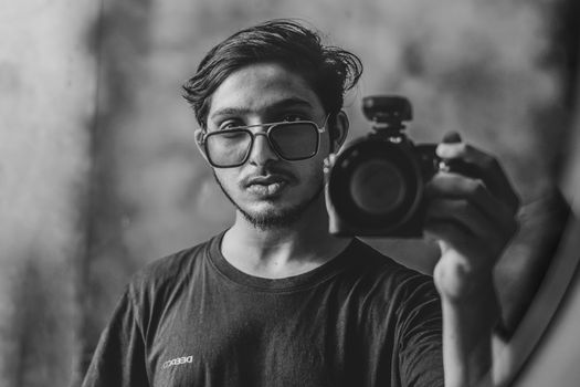 A stylish black and white self-portrait of a man holding a camera, wearing sunglasses.