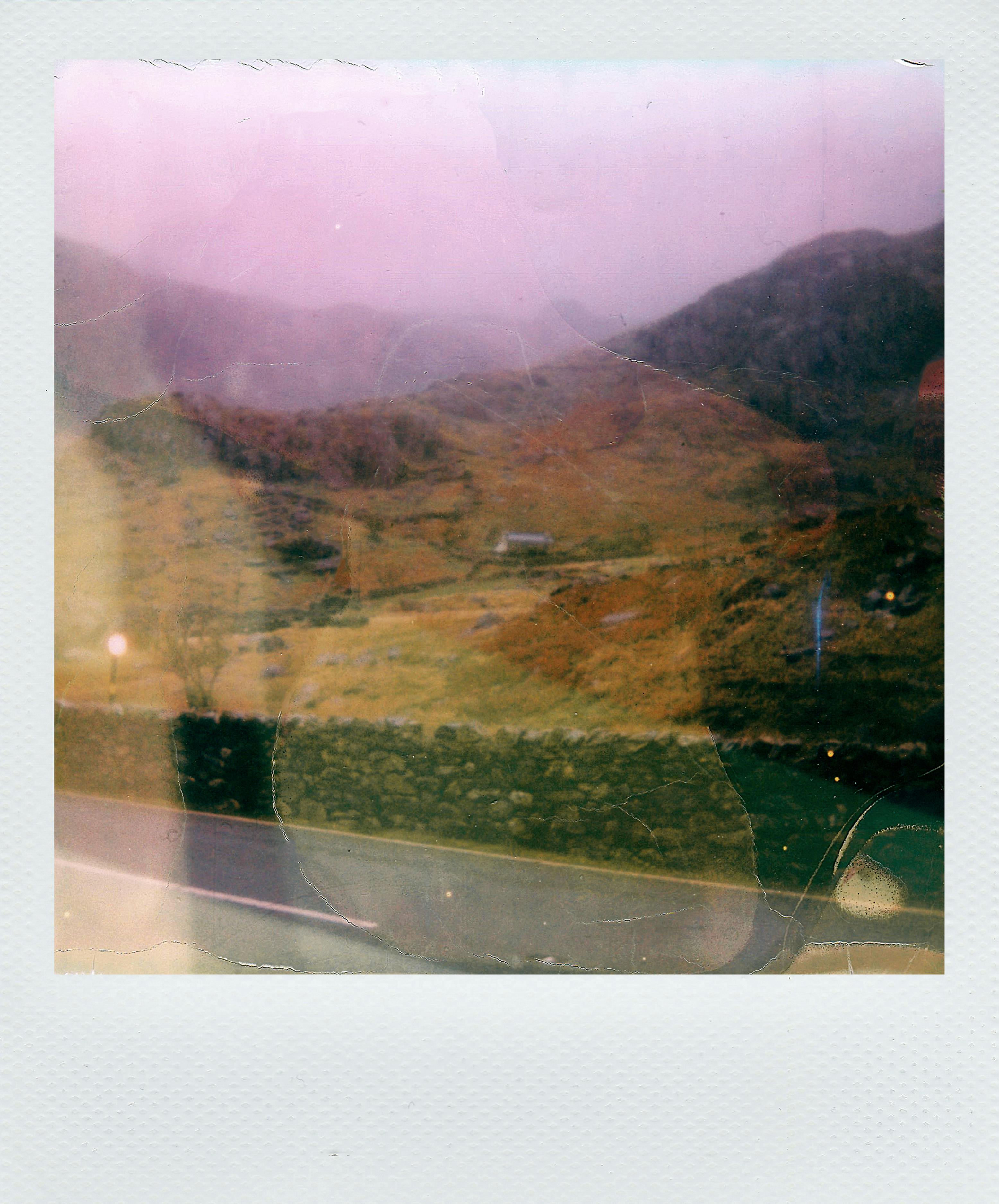 Retro Polaroid photo of a misty hillside in Wales with stone walls, evocative of autumn.