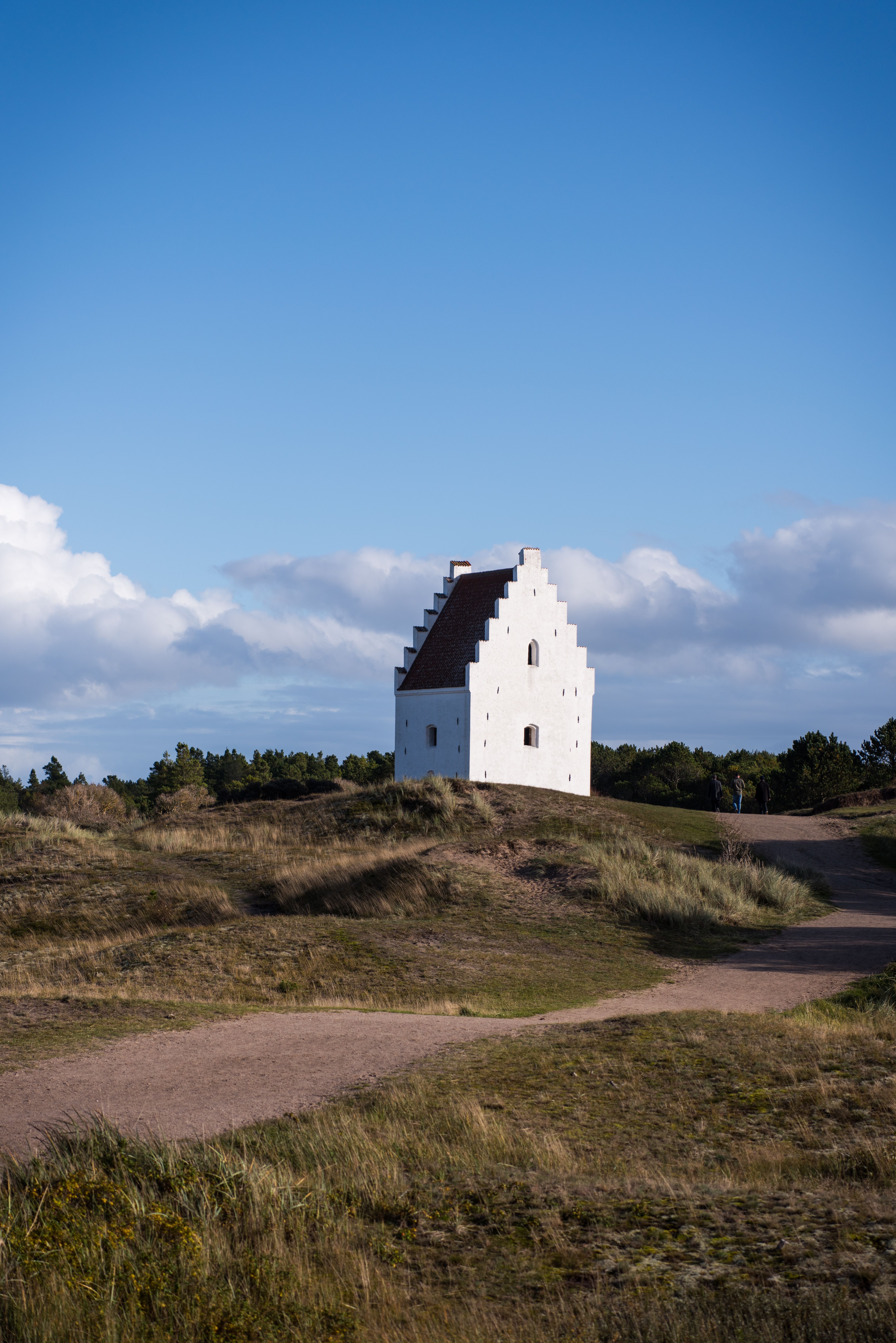 A white church against a blue sky in Skagen, Denmark, surrounded by grassy dunes.