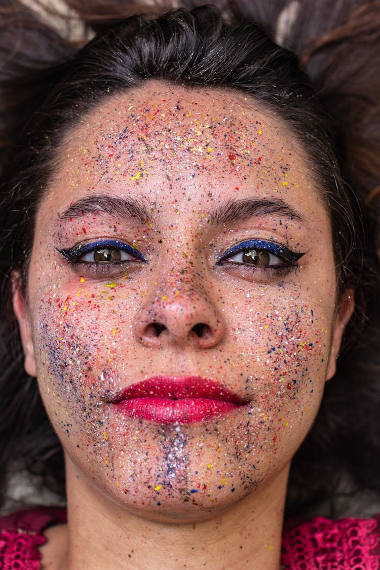 Close-up Shot Of A Woman With Droplets Of Colorful Paint On Her Face Seriously Looking At Camera