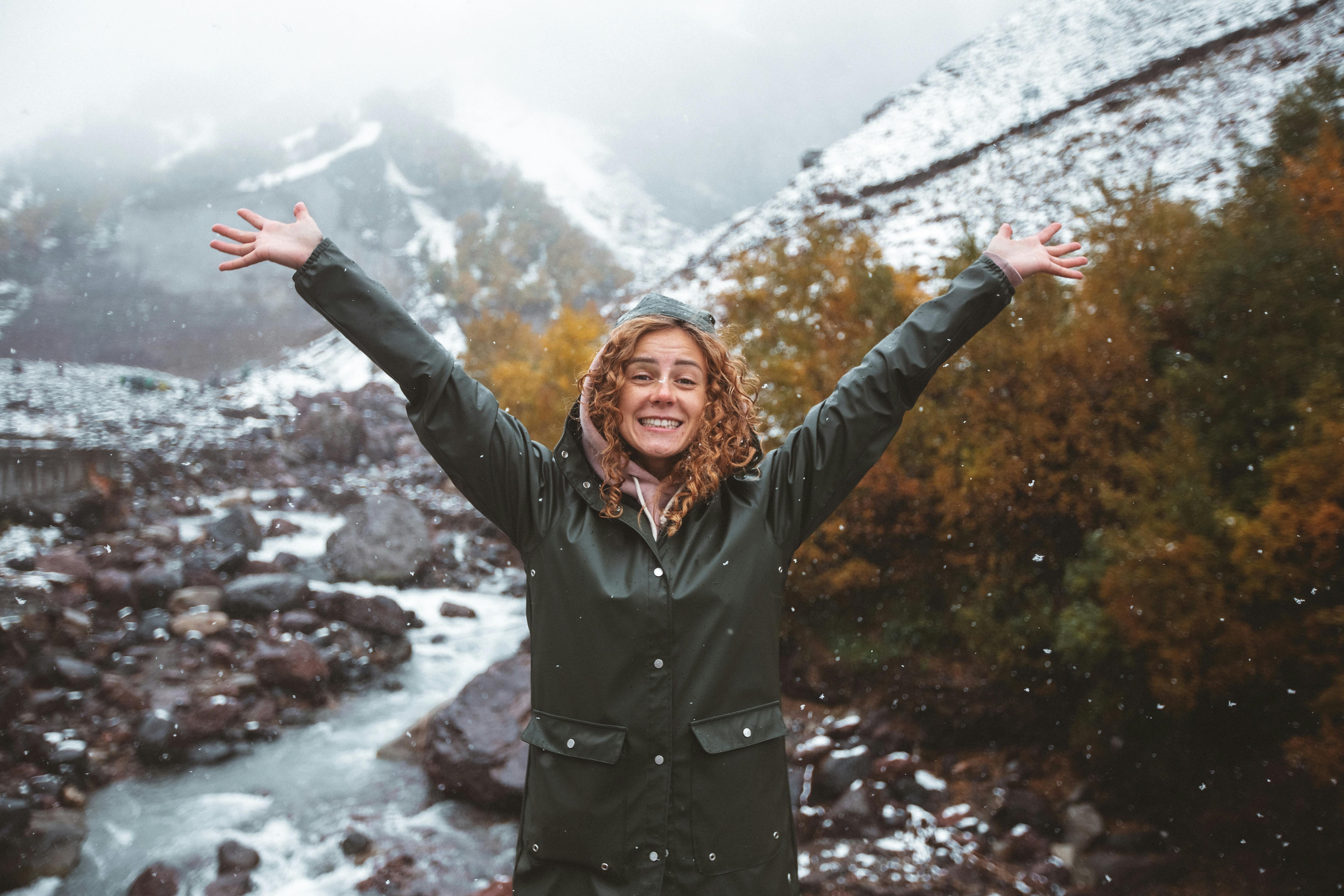 Prescription Goggle Inserts - Happy woman with curly hair in winter attire enjoying snowy mountain scenery outdoors.