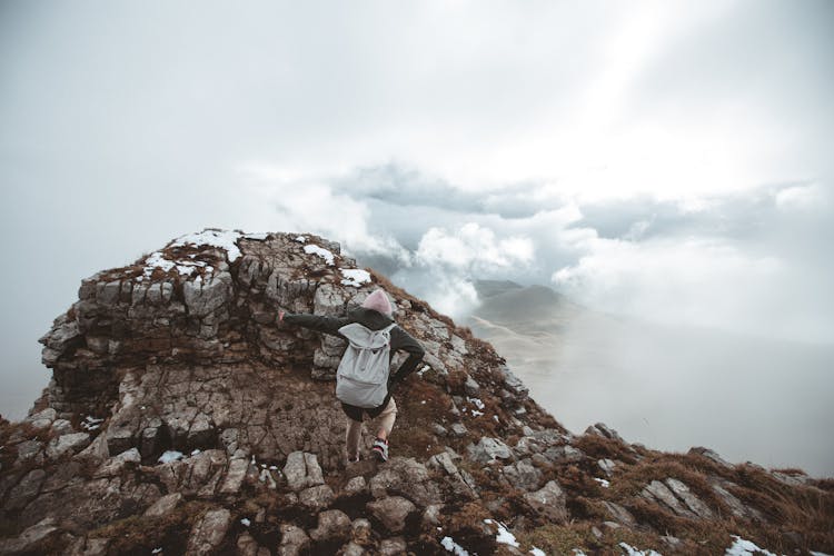A Back View Of A Person Climbing A A Mountain Peak Around Clouds Fog