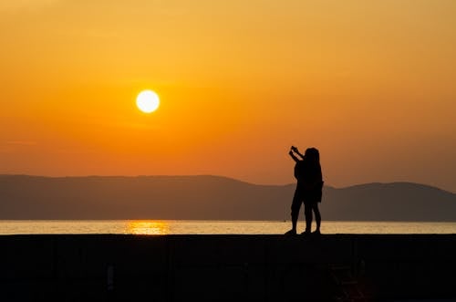 Free Silhouette of People Standing Near Body of Water During Sunset Stock Photo