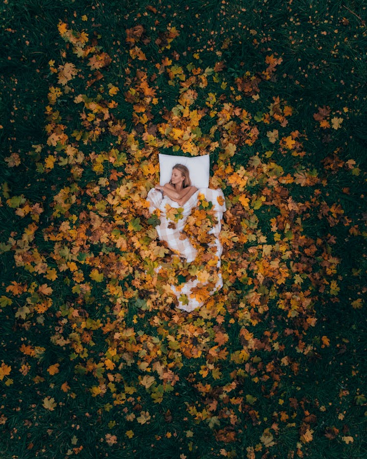 Top View Of A Woman Lying Under A Duvet And Yellow Autumn Leaves