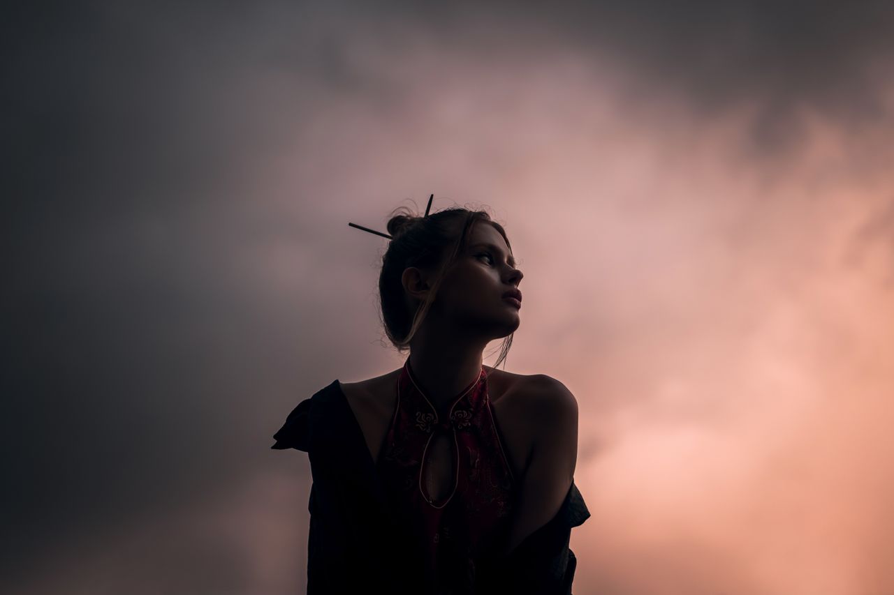 silhouette of a young woman against a dramatic evening sky exuding mys