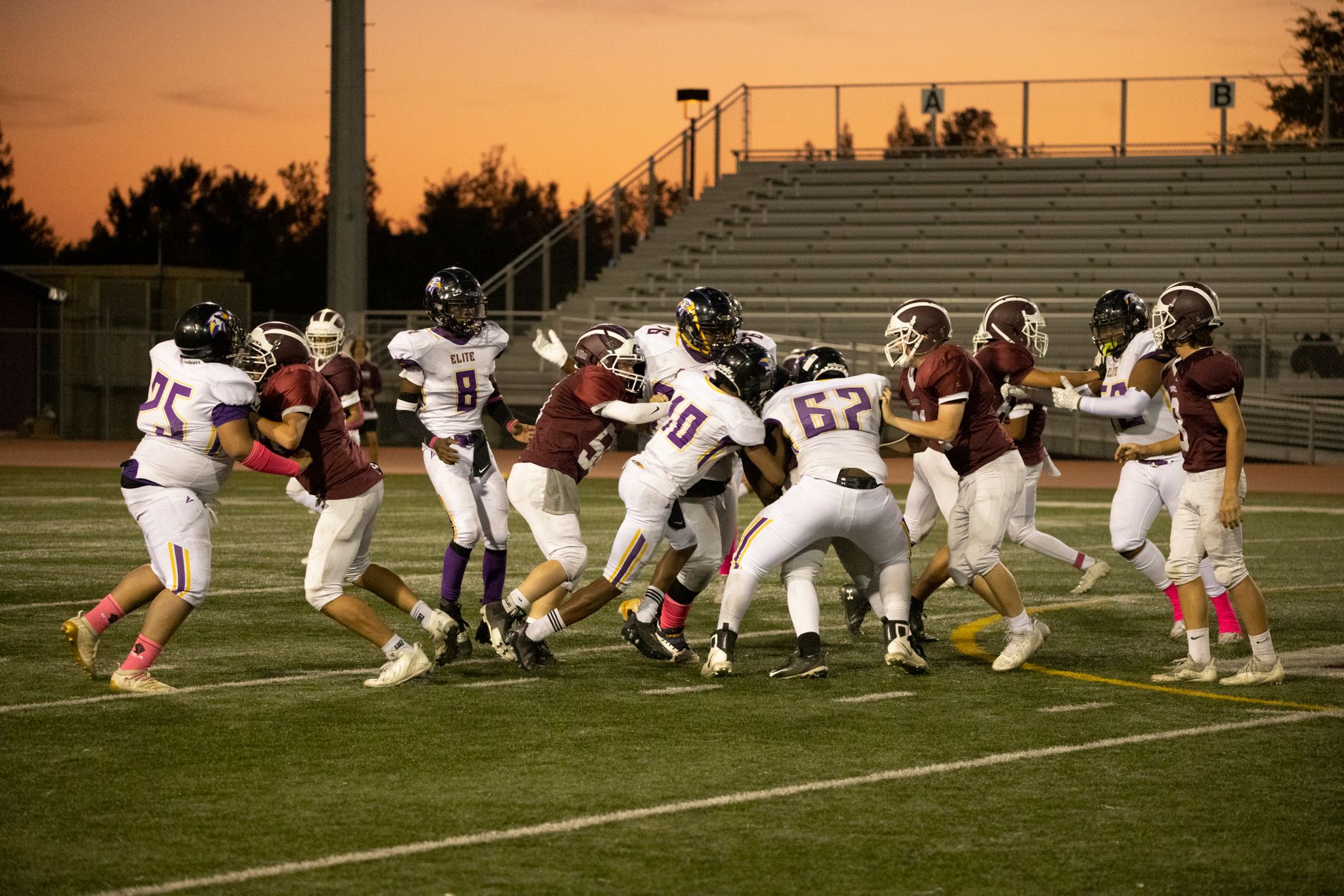Exciting high school football game with players in action on a field at sunset.