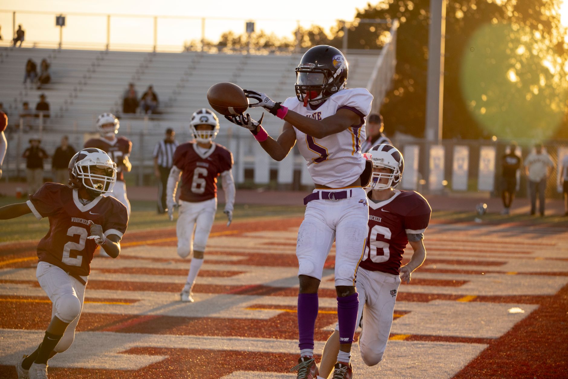 Dynamic action shot of an American football game, capturing midair catch during sunset.