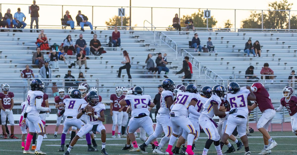 Players compete in a high school American football game with fans in the bleachers.
