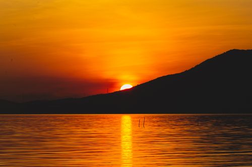 Free Stunning orange sky sunset reflecting on water with mountain silhouette creating a serene seascape. Stock Photo