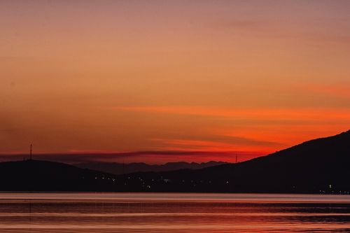 Free Peaceful orange sunset over ocean with silhouetted mountains and a tranquil sky. Stock Photo
