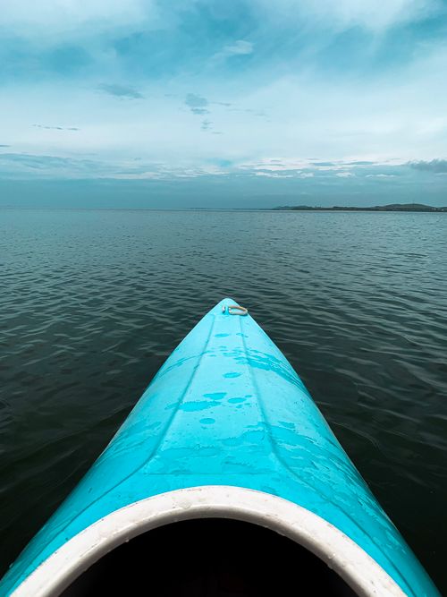 Free Turquoise kayak navigating calm sea under a vast blue sky. Stock Photo