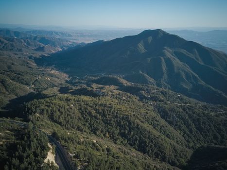 Breathtaking aerial view of lush green mountains and valleys under a clear blue sky.