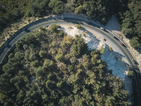 Drone shot of a winding road through a forested area, showcasing nature and transportation.