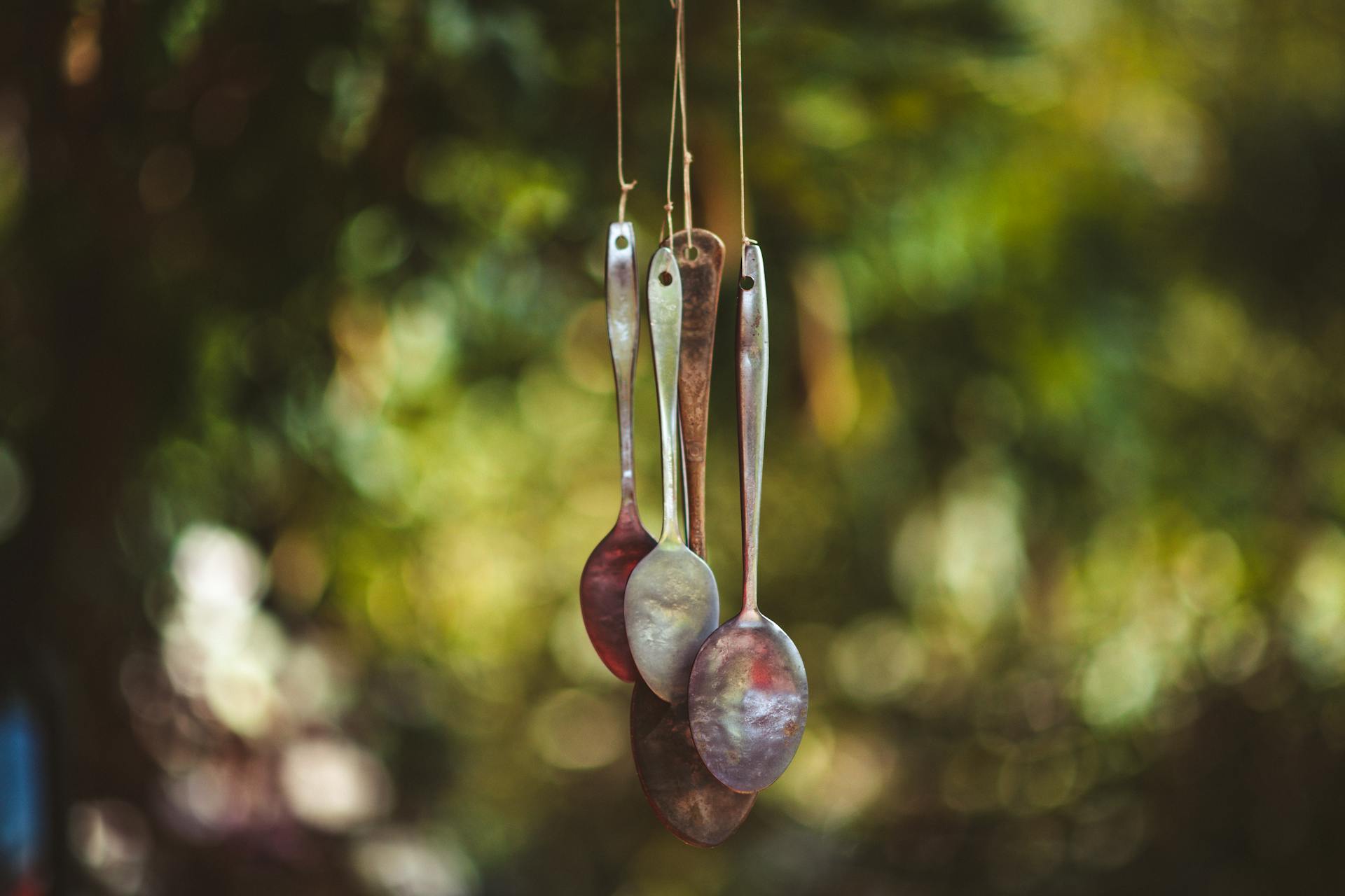 Handmade wind chime made from reused spoons, hanging outdoors with a blurred nature background.