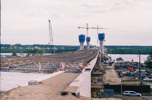A bridge under construction with cranes and river view, showcasing modern infrastructure development.