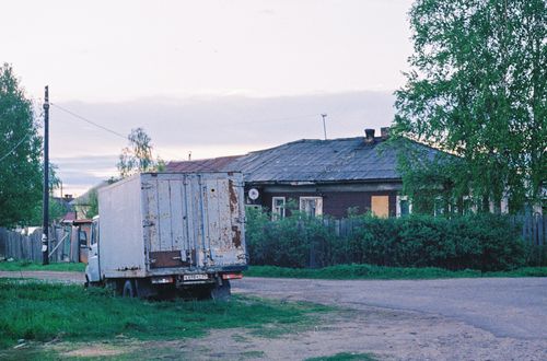 Free A tranquil rural village landscape with an aged truck beside a traditional wooden house on a dirt road. Stock Photo