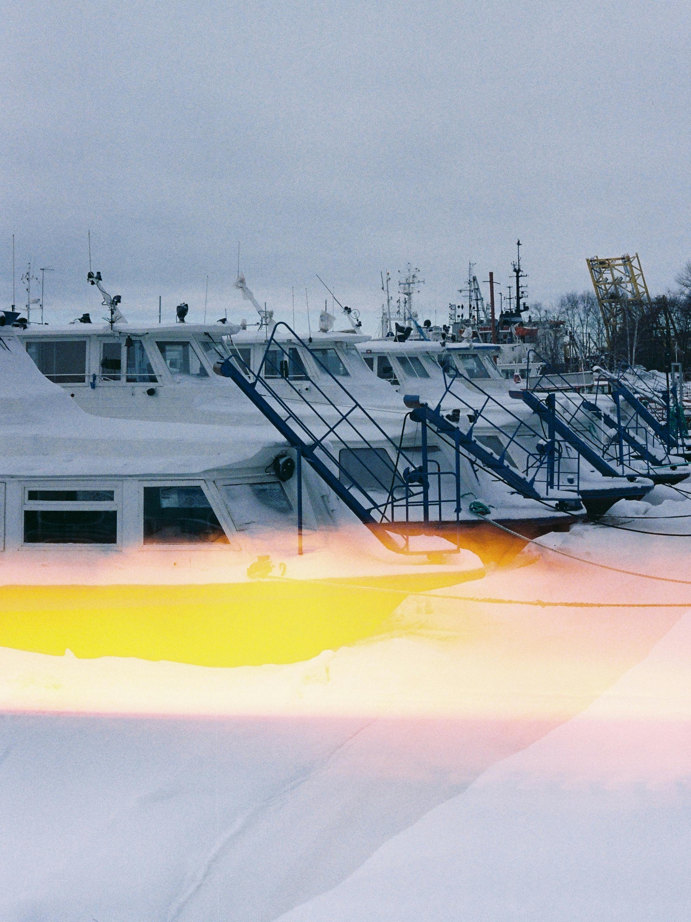 Yachts docked at a winter marina under a gray sky, featuring a striking yellow light leak.
