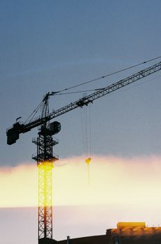 Silhouette of a tower crane against a vibrant sunset sky in an urban setting.