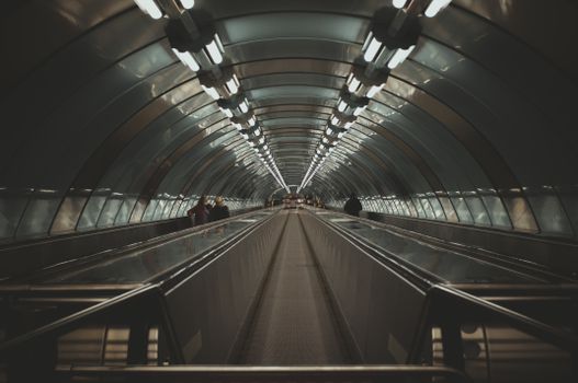 Futuristic underground tunnel featuring a moving walkway and illuminated ceiling.
