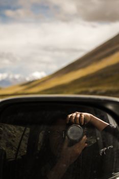 Creative reflection shot of a photographer with camera in car side mirror, blending scenery.