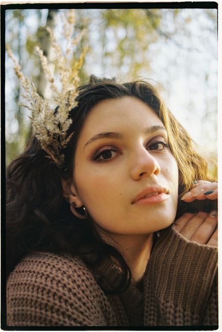 Close up portrait of a woman outdoors wearing a sweater with autumn foliage.