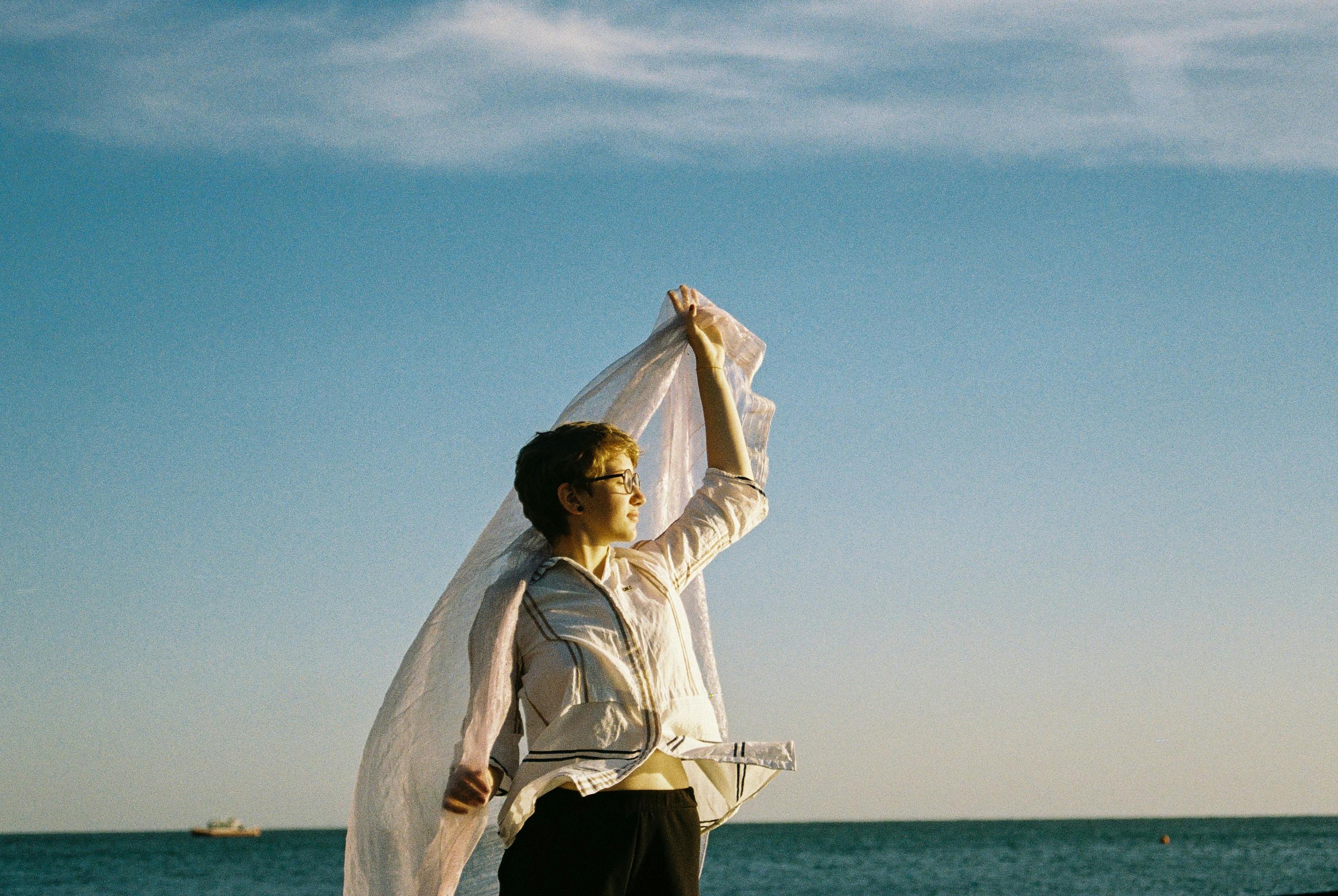 Elegant woman holding a scarf, gazing at the sea during sunrise.