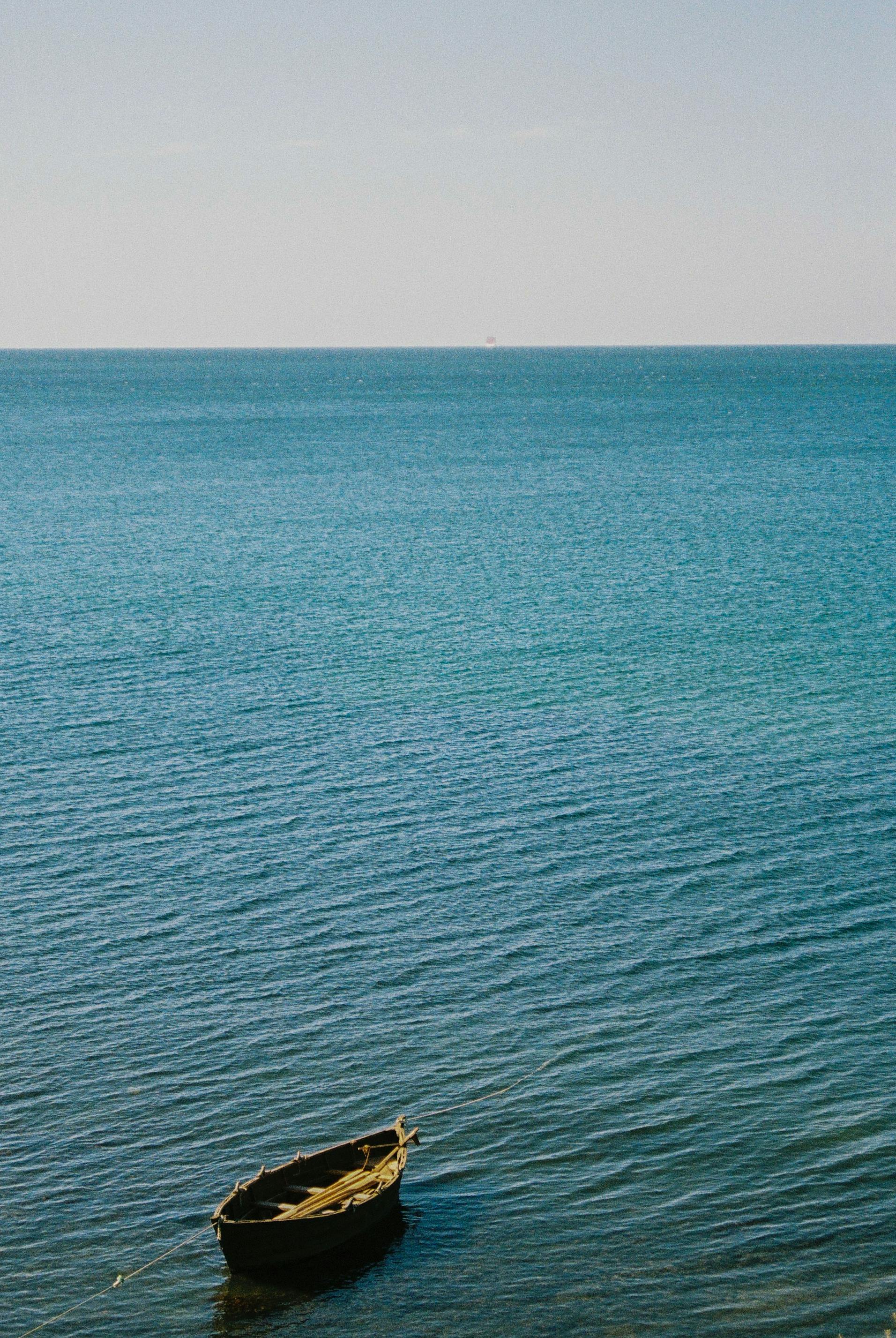 A serene view of a wooden boat floating on the calm sea under a clear sky.