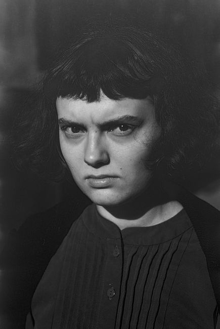 A dramatic black and white portrait featuring a woman with a serious expression and distinctive hairstyle.