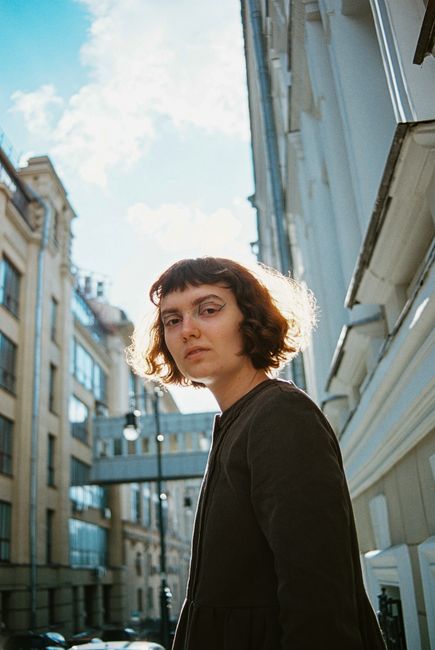 Woman with curly hair stands in sunlight on city street, embodying urban elegance.