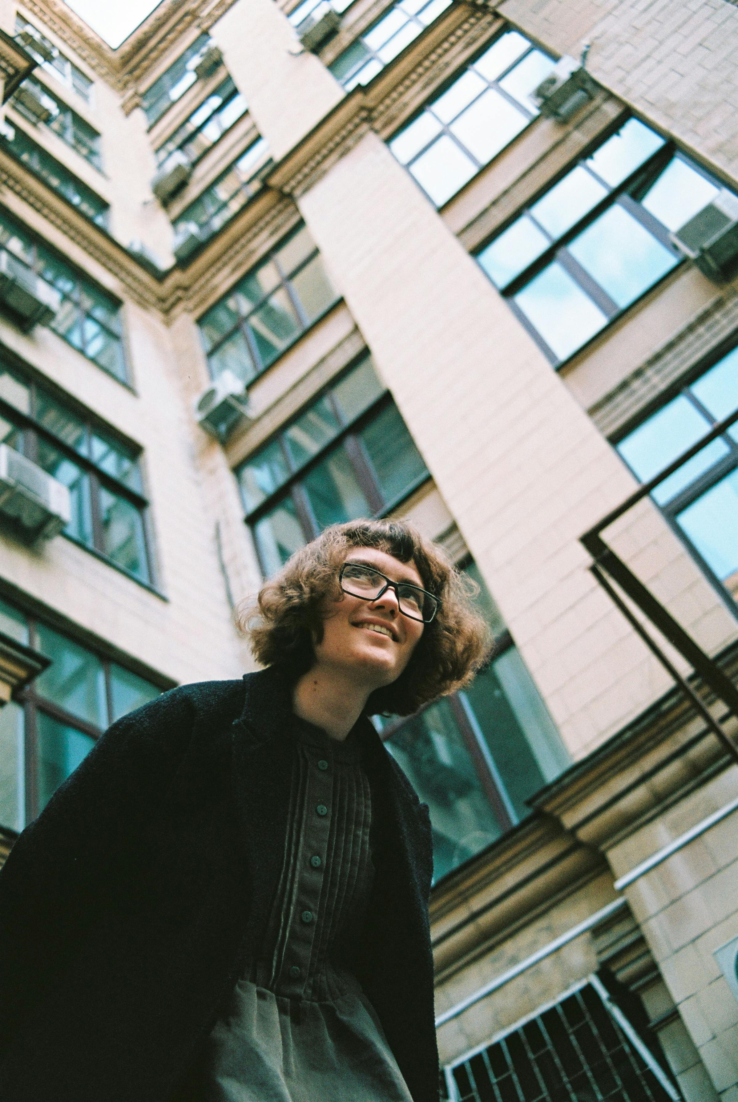 Portrait of a woman smiling with a low angle view of a modern building facade.