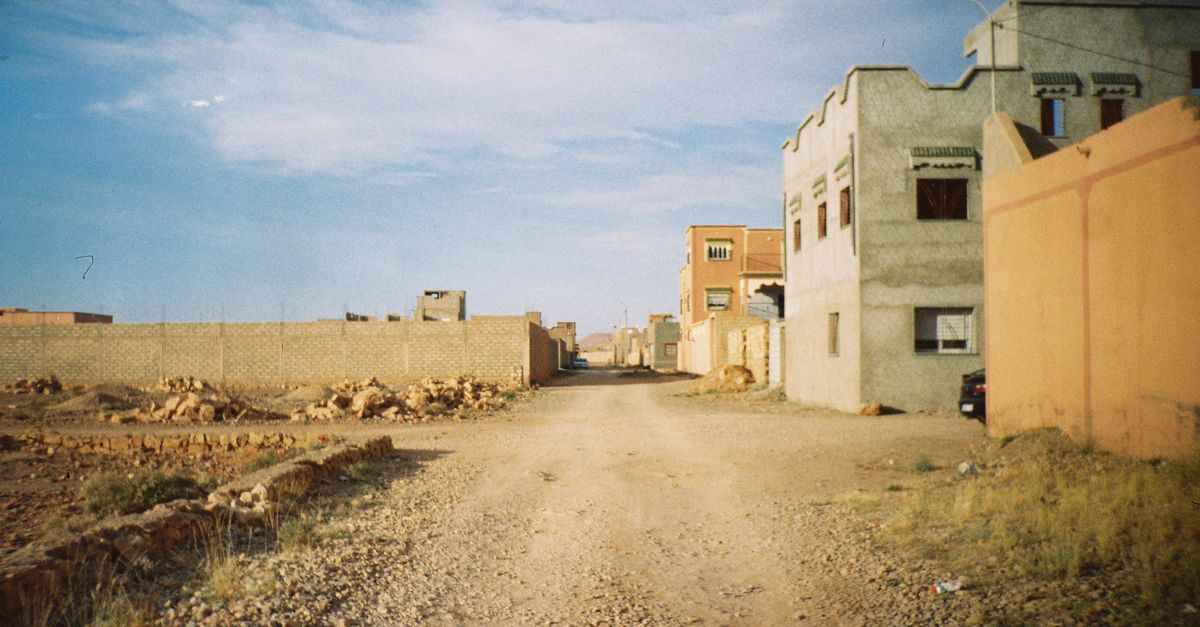 a dusty unpaved road in a Ghanaian neighborhood with a blue gas station in the background