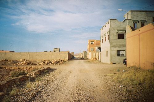 Free Unpaved road in a residential area with concrete buildings under a blue sky. Stock Photo