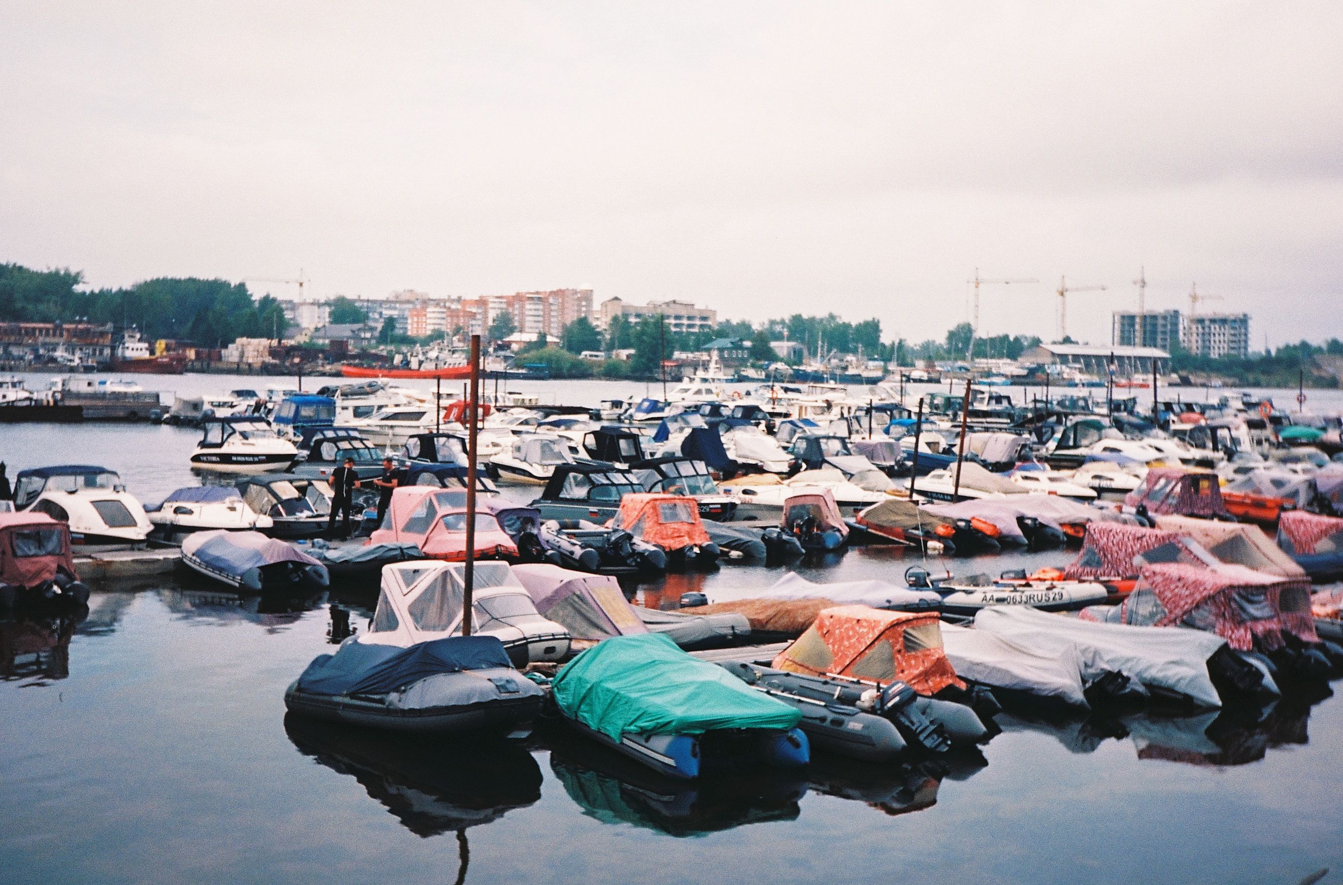 A busy harbor with numerous motorboats docked, featuring a cloudy sky and urban backdrop.