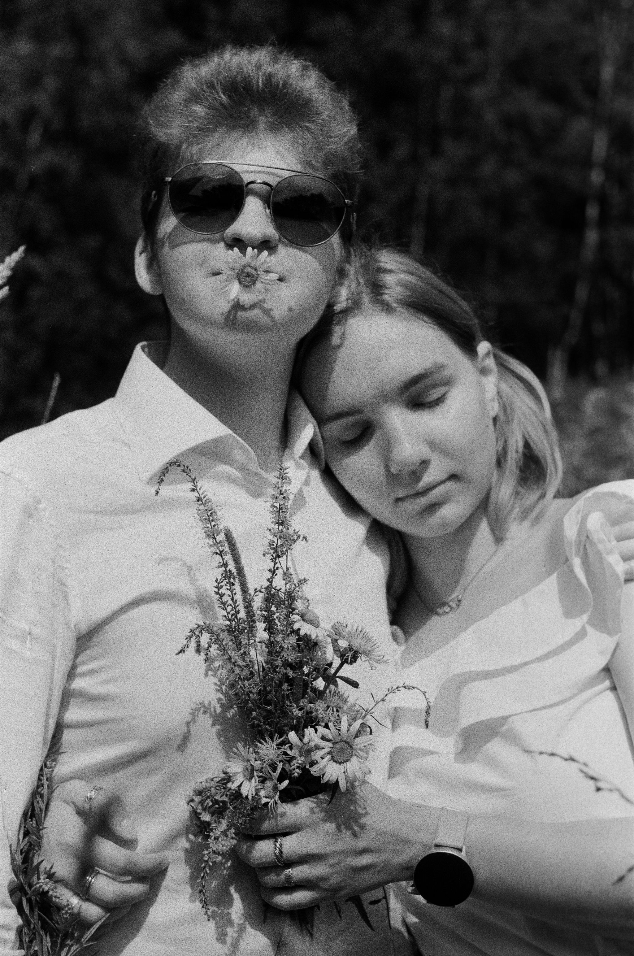 A tender black and white portrait of a couple embracing outdoors, surrounded by nature.