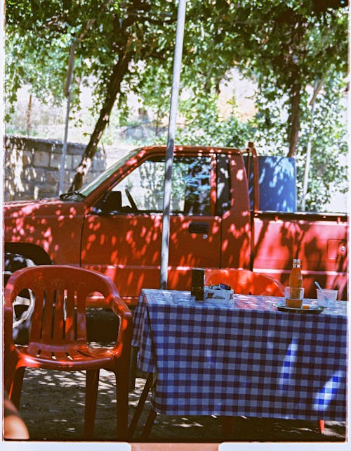 Red Pick-up Truck Near Long Table and Plastic Chair