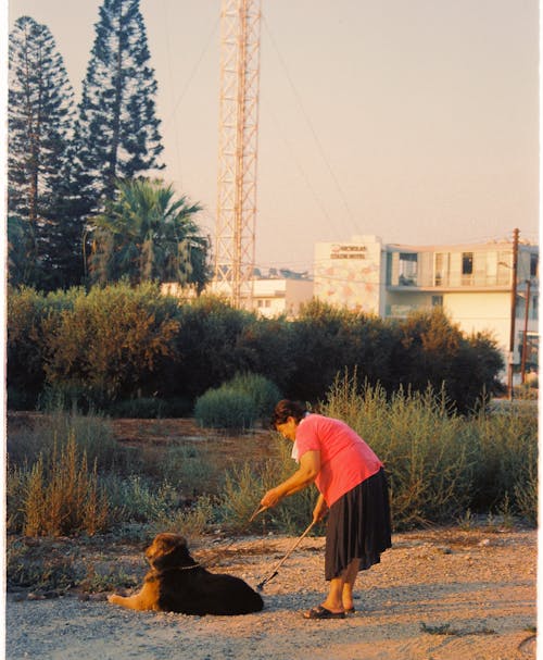 A Woman Standing on an Open Field Beside Black Dog