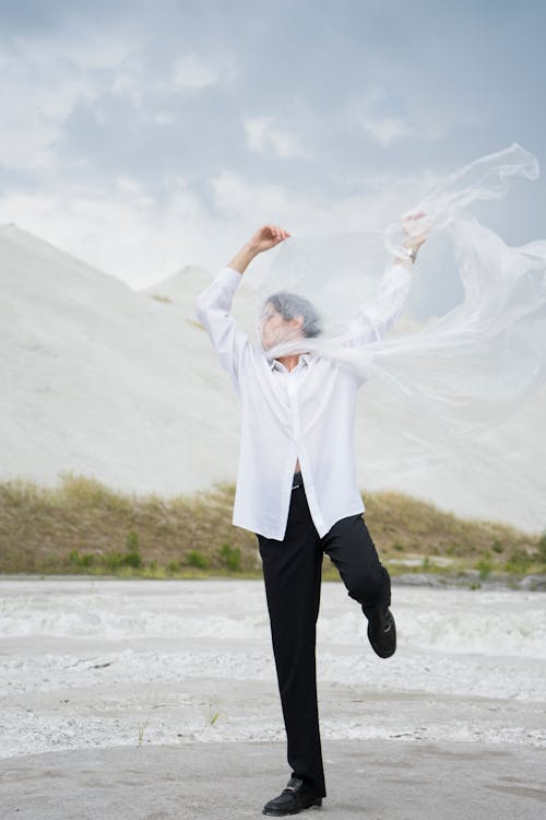 Free Woman in White Long Sleeve Shirt and Black Pants Standing on White Sand Stock Photo